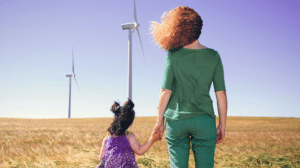 Mutter mit Kind stehen im Getreidefeld und beobachten zwei Windräder, die trotz einer guten Brise nicht drehen.