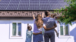Eine Familie steht vor ihrem Haus mit einer frisch installierten Photovoltaik-Anlage auf dem Dach.