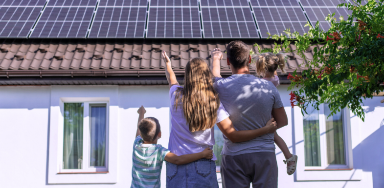 Eine Familie steht vor ihrem Haus mit einer frisch installierten Photovoltaik-Anlage auf dem Dach.